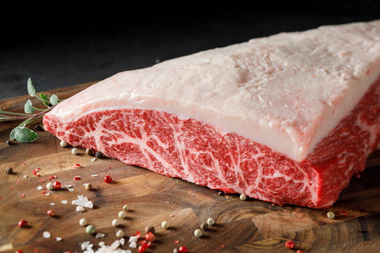 Raw, marbled, wagyu beef on a wooden cutting board with spices.  Product is a Wagyu Picanha (Coulotte)