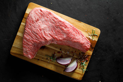 Raw Sirloin Tri-Tip steak on a wooden cutting board with herbs and onions on a dark background