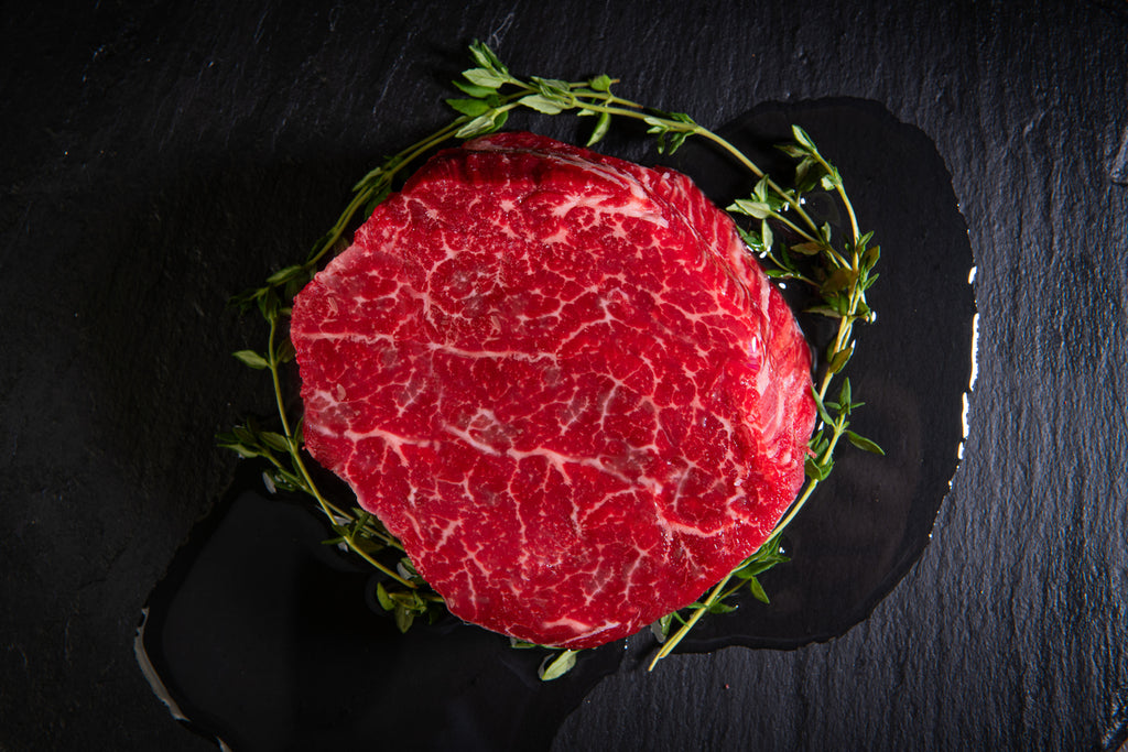 Raw (baseball cut) Top Sirloin Steak with greenery on a dark slate surface