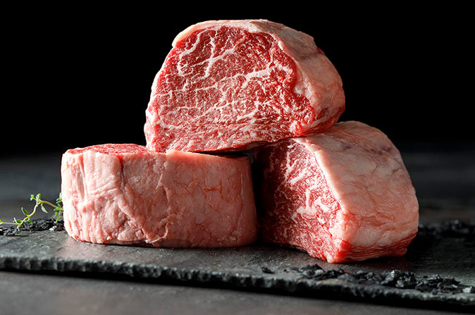 Three pieces of raw beef on a dark slate surface with a black background